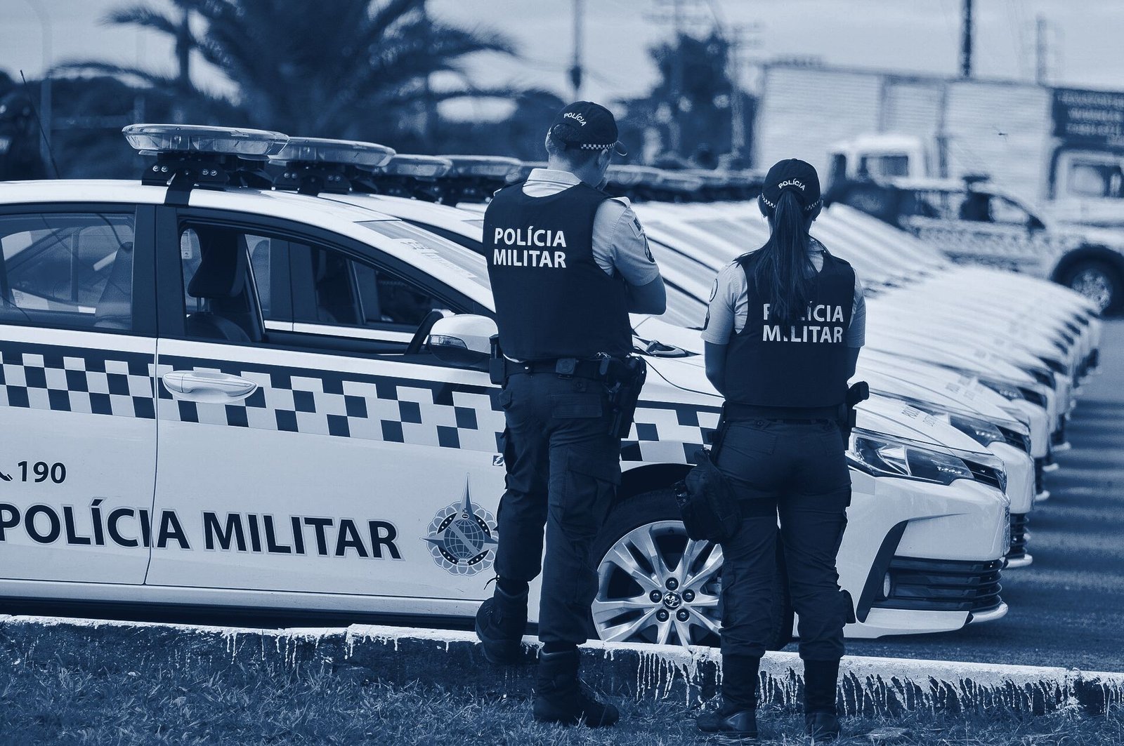 Dois policiais militares do DF de costas, diante de uma fileira de viaturas